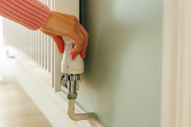 Close-up on a woman's hand adjusting thermostat valve on a heating radiator. Energy crisis and cold weather concept