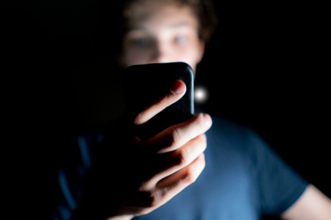 young attractive man use mobile phone late at night in a dark room