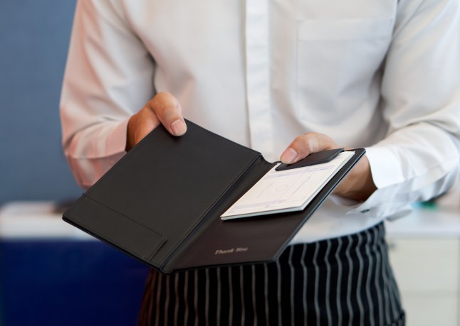 A waiter in a white shirt and apron presenting the bill in a restaurant.