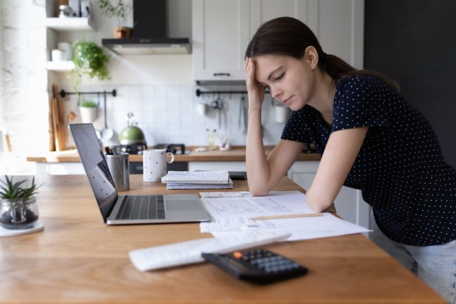 Concerned young woman thinking over domestic paperwork, sitting at laptop computer, papers, calculator at home, touching face, head, analyzing bills, taxes, expenses, financial problems; Shutterstock ID 2156291003; purchase_order: -; job: -; client: -; other: - 14667071