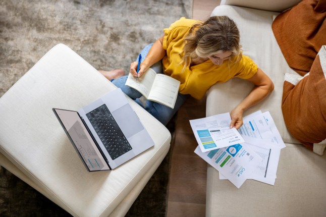 English woman at home paying bills online using her laptop while sitting on the ground - home finances concepts