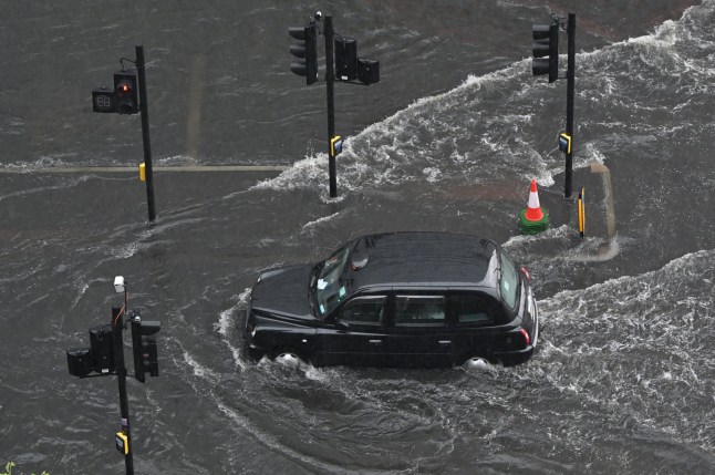 TOPSHOT - A London taxi drives through water on a flooded road in The Nine Elms district of London on July 25, 2021 during heavy rain. - Buses and cars were left stranded when roads across London flooded on Sunday, as repeated thunderstorms battered the British capital. (Photo by JUSTIN TALLIS / AFP) (Photo by JUSTIN TALLIS/AFP via Getty Images)