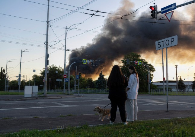 Women walk dog as smoke rises over Kyiv following mass Russian drones and missile strikes on the Ukraine's capital on July 4, 2025, amid the Russian invasion of Ukraine. Ukraine said Russia had launched 550 drones and missiles at the war-battered country overnight, as the Kremlin steps up aerial attacks and US-led peace talks stall. The Ukrainian air force said Moscow had launched 539 drones and 11 missiles, adding that air defence units had downed 268 drones and two missiles. (Photo by OLEKSII FILIPPOV / AFP) (Photo by OLEKSII FILIPPOV/AFP via Getty Images)
