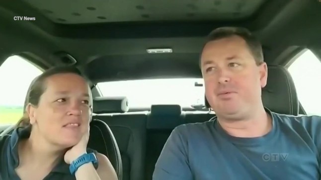A man and a woman sitting in the front seats of a car facing the viewer