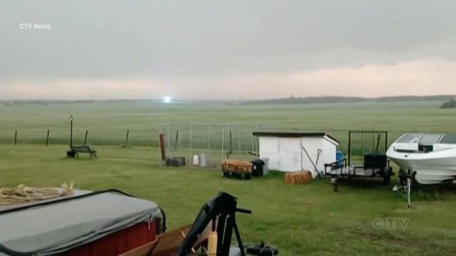 A field with vehicles in the foreground and a large ball of blue-white light hovering in the distance