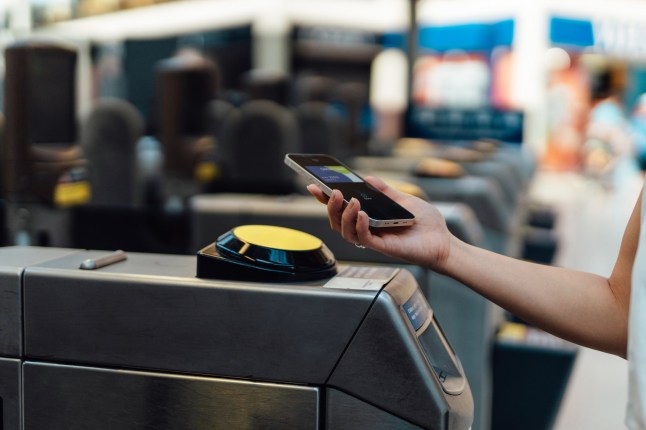 Cropped shot of young woman holding mobile device close to the payment terminal at the entrance of Tube station.