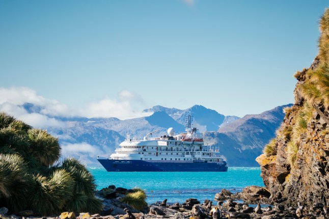 A cruise ship sailing off Jason Harbour, surrounded by mountains and blue sea, on a bright day.