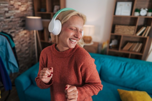 Happy young woman listening to headphones to illustrate lossless audio is coming on Spotify
