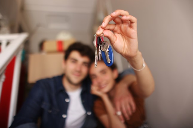 A smiling young couple holding up a set of keys.