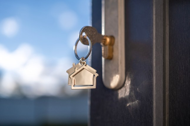A close up of a key in a lock with a silver keyring in the shape of a house attached.