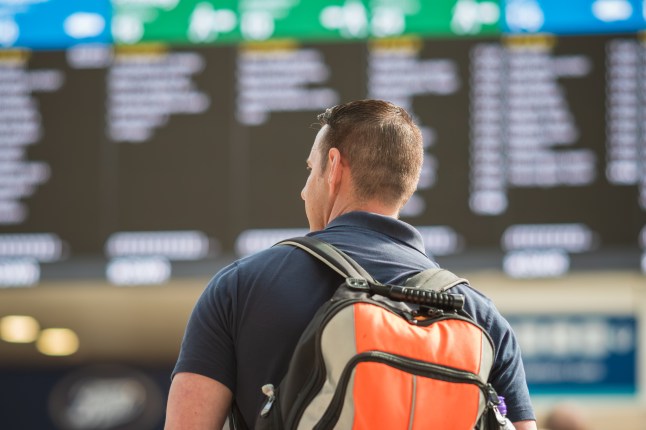 A male passenger at London Waterloo station with train departure board blurred in the background