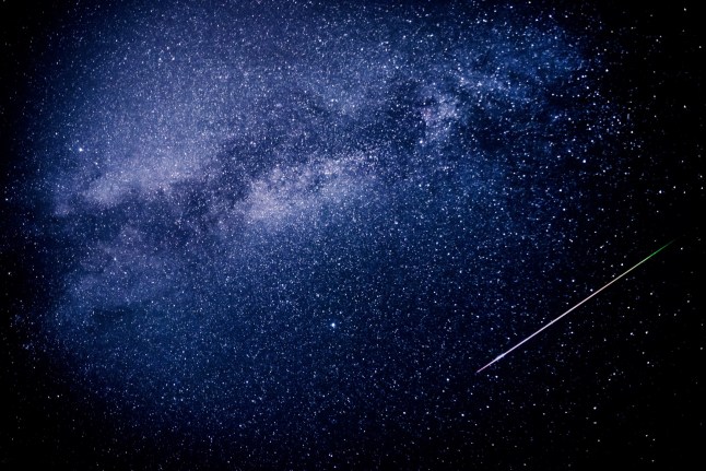 A meteor shoots across the night sky sky leaving a trail of light across the milky way