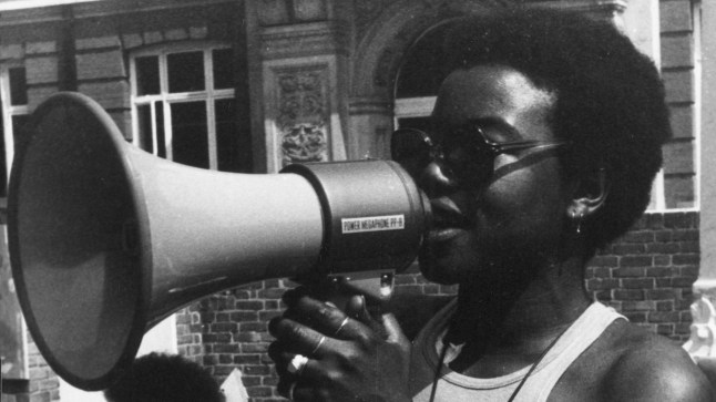 BHM logo: Olive Morris is speaking into a megaphone in a black and white image