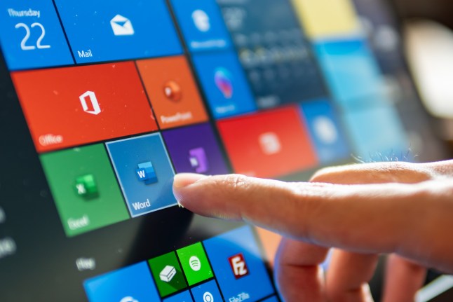 Close-up of someone pushing their finger against a touchscreen showing Microsoft apps including Word, Excel and PowerPoint