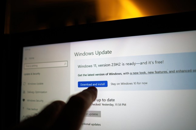 Finger pointing to the Windows Update screen on a laptop, highlighting the Download and install button for Windows 11