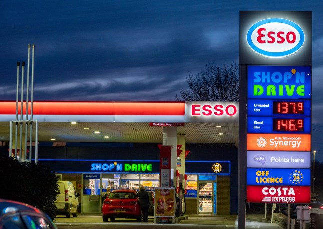 Photo of an Esso petrol station at night showing a sign displaying fuel prices