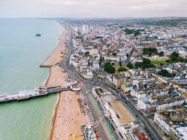 Aerial view of Brighton beach and the pier on a cloudy day with the i360, old piers and Hove visible in the distance.