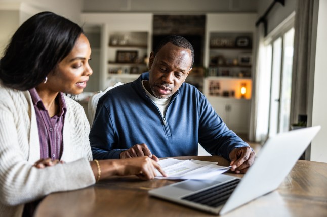 Husband and wife looking over bills and using laptop in domestic kitchen