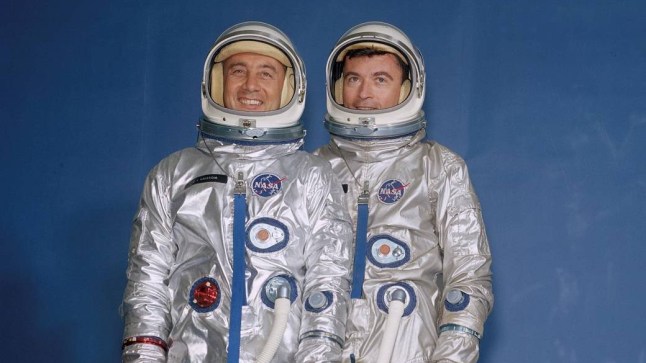 Gemini III crew members Virgil I. "Gus" Grissom (left) and John W. Young are wearing their spacesuits, helmets and portable air conditioners.