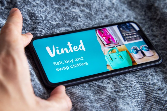 Vilnius, Lithuania - November 06, 2020; Vinted Iphone screen with vinted logo on screen with hand on vintage wooden background. Vinted is a Lithuanian online marketplace. #Vinted; Shutterstock ID 1891017088; purchase_order: -; job: -; client: -; other: -