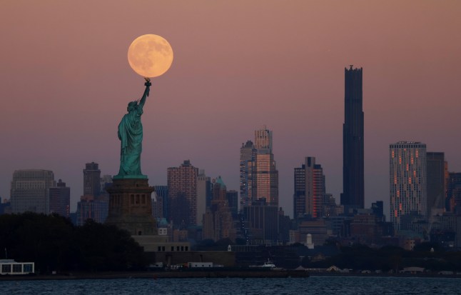 JERSEY CITY, NJ - OCTOBER 6: The Harvest Supermoon rises behind the Statue of Liberty and the Brooklyn skyline in New York City as the sun sets on October 6, 2025 as seen from Jersey City, New Jersey. (Photo by Gary Hershorn/Getty Images)