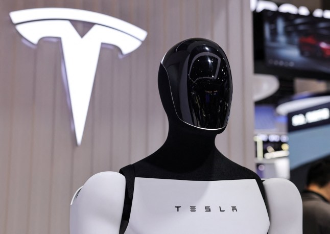 A Tesla Optimus robot is displayed next to a logo at the company???s booth at the 8th China International Import Expo (CIIE) in Shanghai, China, November 6, 2025.REUTERS/Maxim Shemetov