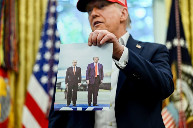 US President Donald Trump holds a photo of himself with Russian President Vladimir Putin in Alaska, while speaking in the Oval Office of the White House in Washington, DC, US, on Friday, Aug. 22, 2025. Trump announced that Washington's John F. Kennedy Center for the Performing Arts will host the draw for the 2026 FIFA World Cup. Photographer: Annabelle Gordon/UPI/Bloomberg via Getty Images