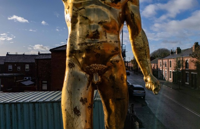 Aerial images of a controversial 20-foot-tall nude statue banned by a local council which has been reinstated - after a campaign by dozens of locals. The striking gold Roman Gladiator statue - once used to promote the Russell Crowe blockbuster in 2000 - was re-erected at Bulldog Forge, in Ince, Wigan, Greater Manchester, earlier this week (Nov 26). A controversial 20-foot-tall nude statue banned by a local council has been reinstated - after a campaign by dozens of locals. The striking gold Roman Gladiator statue - once used to promote the Russell Crowe blockbuster in 2000 - was re-erected at Bulldog Forge, in Ince, Wigan, Greater Manchester, earlier this week (Nov 26).The much-loved figure - known to locals as 'Golden Balls' - was taken down on October 11 2022 after Wigan Council ordered its removal following a number of complaints from neighbours.The decision caused backlash in the community who later set up Facebook pages and petitions for him to be returned. Photo released 30/11/2025