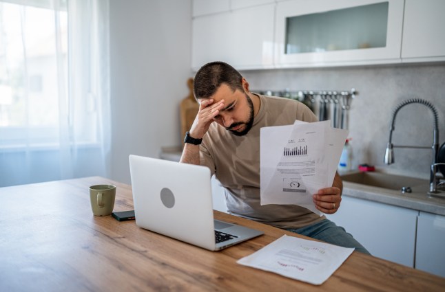 Man stressed at home calculating bills on laptop