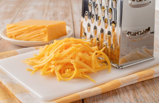 Grated cheddar cheese close-up. Shredded cheese and grater on a white cutting board over rustic wooden tabletop.