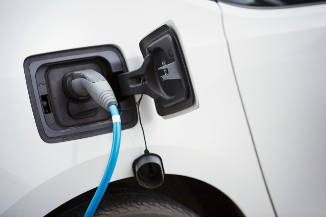 Close up of electric car being charged by a blue cable plugged in, topping up the battery.