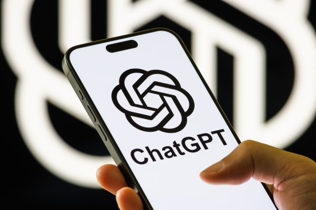 CHONGQING, CHINA - AUGUST 9: In this photo illustration, a person holds a smartphone displaying the ChatGPT logo on its screen in front of a blurred OpenAI logo on August 9, 2025 in Chongqing, China. (Photo illustration by Cheng Xin/Getty Images)