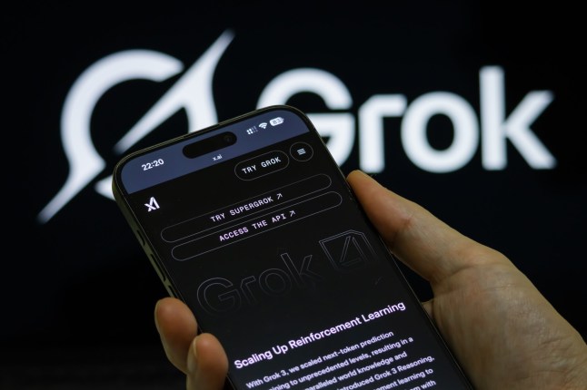 CHONGQING, CHINA - JULY 16: In this photo illustration, a person holds a smartphone showing the Grok 4 introduction page on the official website of xAI, the artificial intelligence company founded by Elon Musk, with the Grok logo visible in the background on July 16, 2025 in Chongqing, China. (Photo by Cheng Xin/Getty Images)