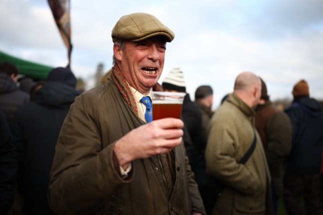 TOPSHOT - Reform UK leader, Nigel Farage enjoys a beer as he mixes with members of the public waiting at Chiddingstone Castle for the arrival of the Old Surrey, Burstow and West Kent Hunt, before they take part in the annual Boxing Day hunt, in Chiddingstone, south of London on December 26, 2025. (Photo by HENRY NICHOLLS / AFP via Getty Images)